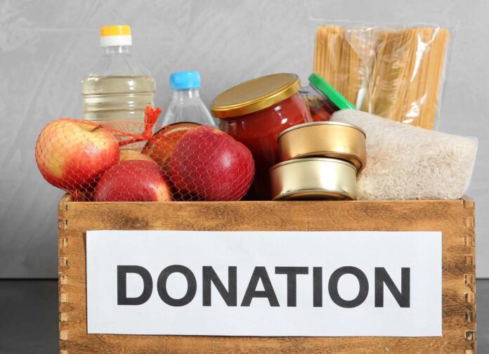 Donation box with food on table against light background. Space